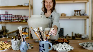 Frau greift nach Pinseln im Kunststudio.