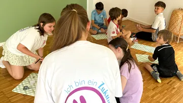 Kinder sitzen am Boden mit Bastelarbeiten.