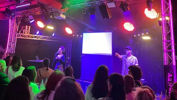 Two performers on stage, colorful lights, audience watching.