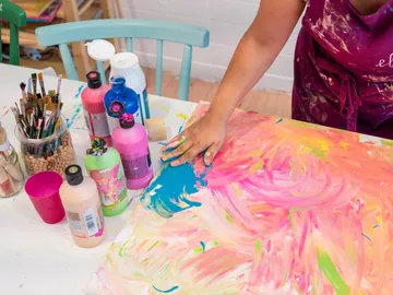 A hand paints on a canvas with blue paint.