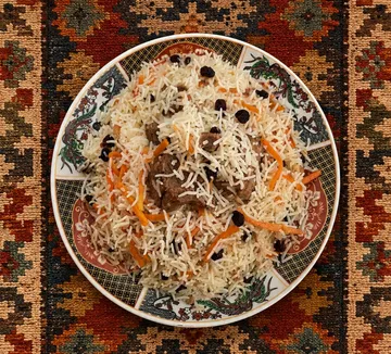 Teller mit Reis und Fleisch auf buntem Stoff.