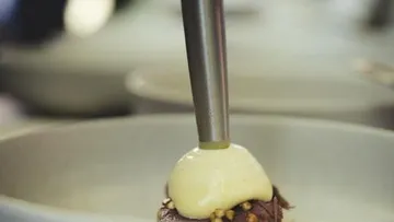 Chef piping sauce on meat dish.