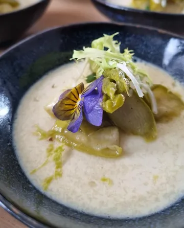 Garnished soup with purple flower, black bowl.