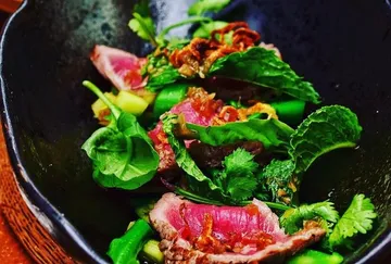 Seltenes Rinderfleisch mit Gemüse in schwarzer Schüssel.