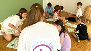 Children sitting on floor, crafting in classroom.