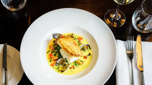 Teller mit Fisch und Muscheln in Sauce, Restaurantumgebung.