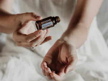 One hand holds a bottle of peppermint oil over another hand.