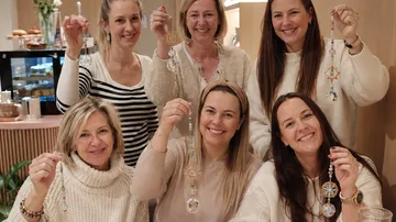 Women displaying handmade beaded ornaments indoors.