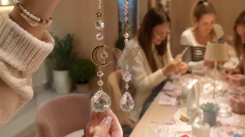 Hand hält Kristalldekorationen; Frauen basteln am Tisch.