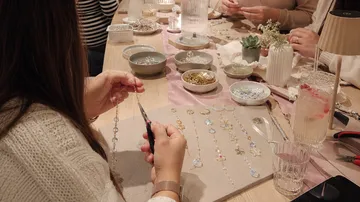 Woman crafting jewelry at a table.