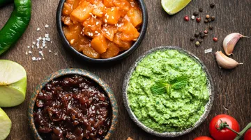 Three bowls with dips, surrounded by ingredients.