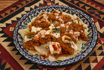 Gericht mit Teigtaschen, Soße, Joghurt auf Dekoteller.