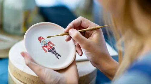 Person painting a nutcracker on ceramic plate.