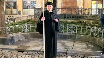 Person in historischer Kleidung mit Stock, draußen.
