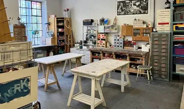 Kunststudio mit Tischen, Regalen und Kunstbedarf.