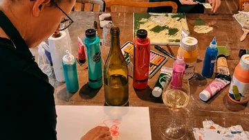 Person malt an einem Tisch mit Kunstmaterialien.