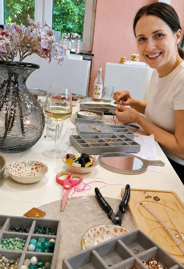 Woman making jewelry at a table indoors.