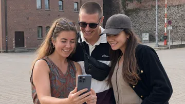 Drei Personen lächeln auf ein Telefon draußen.