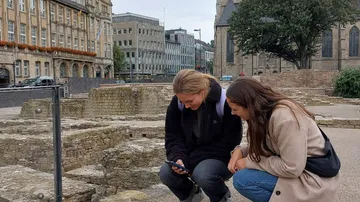 Zwei Personen schauen auf Handy über Ruinen.