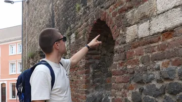 Person zeigt auf antike Ziegelwand im Freien.