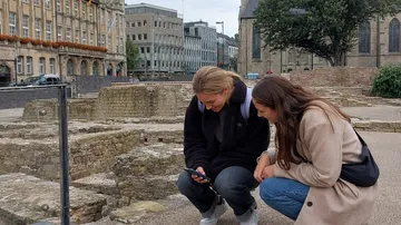 Zwei Frauen sehen draußen auf ein Handy.