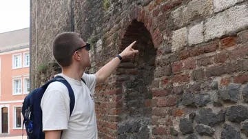 Mann zeigt auf historische Backsteinmauer.