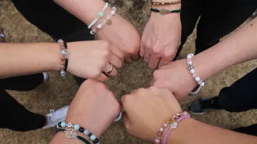 Mehrere Hände mit Perlenarmbändern, Fäuste zusammen im Freien.
