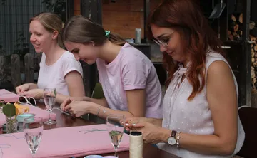 Three women embroidering at a table outside.