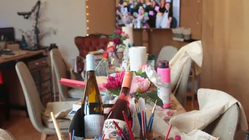 Table with paint supplies and wine bottles.