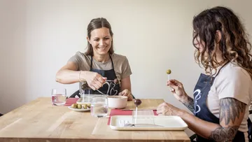 Two women dining, holding olive sticks.