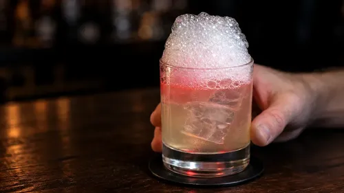 Glas mit rosa schaumigem Getränk auf Tisch.