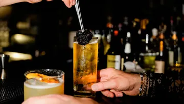 Hände halten Cocktailgläser an einer Bar.