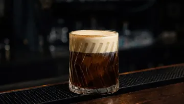 Glas mit schaumigem Getränk auf dunkler Bar.