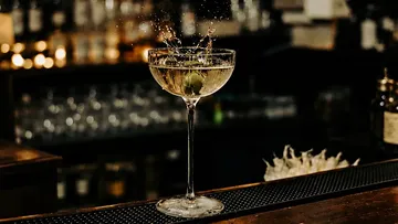 Cocktailglas mit Olivenspritzer auf Bartheke.