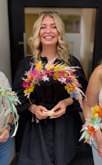 Woman holding colorful flower crown indoors.