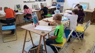 Kinder malen an Klassenzimmertischen.