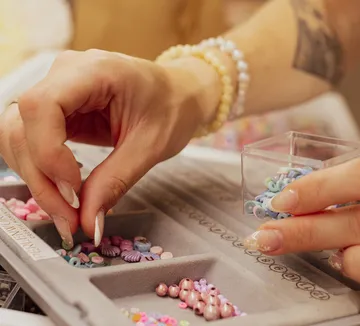 Hands sorting colorful beads in tray.