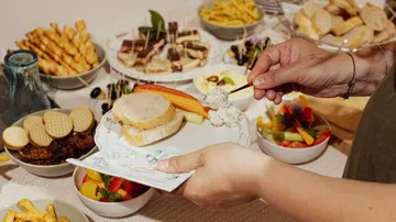 Hands plating food at a buffet.