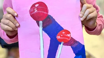 Hands holding painting of two lollipops.