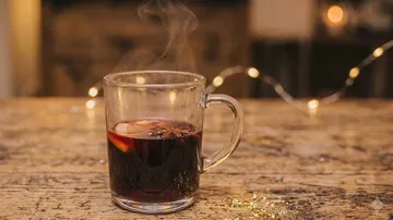 Glasbecher mit dampfendem Glühwein auf Tisch.