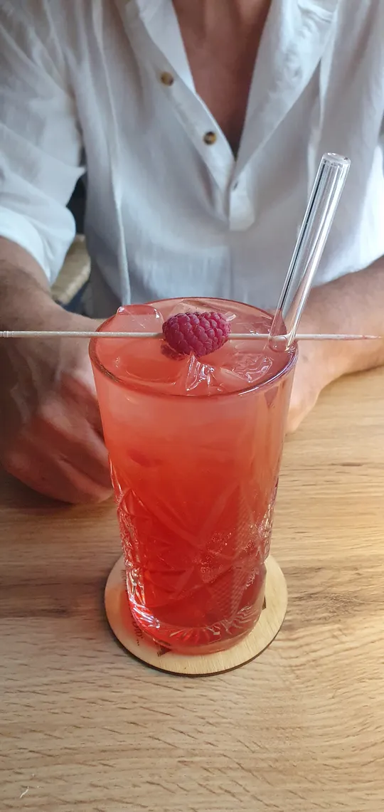 Roter Cocktail mit Himbeere auf Tisch.