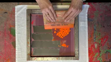 Hands spreading paint on screen printing frame.