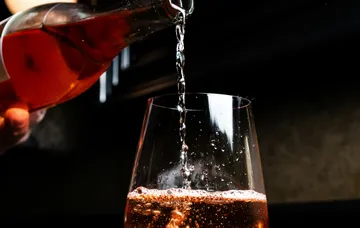 Wine being poured into a glass, dark background.