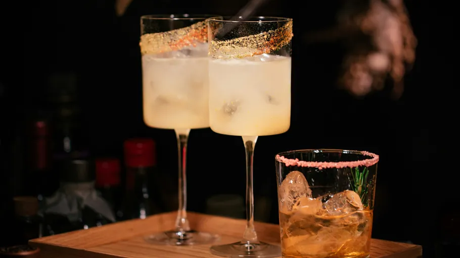 Three cocktails with ice on a wooden tray.