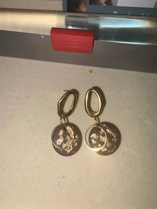 Goldene Ohrringe mit braunen Scheiben auf Tisch.