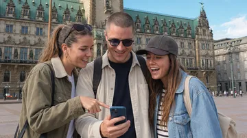 Three friends looking at phone outside building.