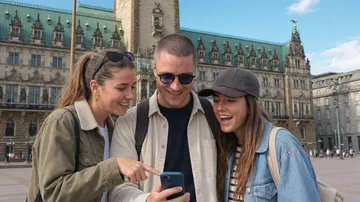 Drei Personen lachen beim Handy im Freien.
