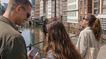 Personen schauen auf Smartphone am Kanal.