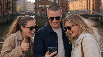 Drei Freunde lachen über ein Handy am Kanal.