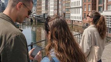 Drei Personen schauen auf Handy am Kanal.